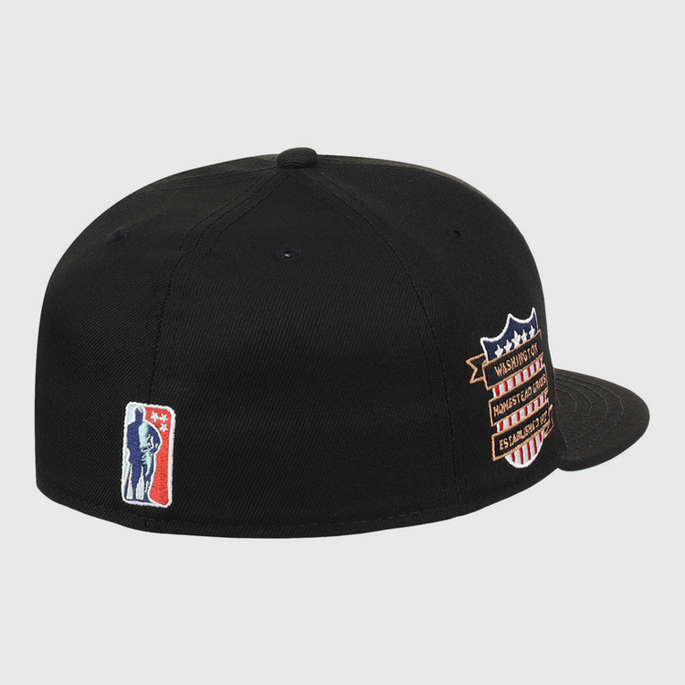 The Ebbets Field Homestead Grays NLB Tc Fitted Ballcap is a black cap featuring a small blue and white basketball player silhouette embroidered on the back and a multicolored shield patch with text on the side.