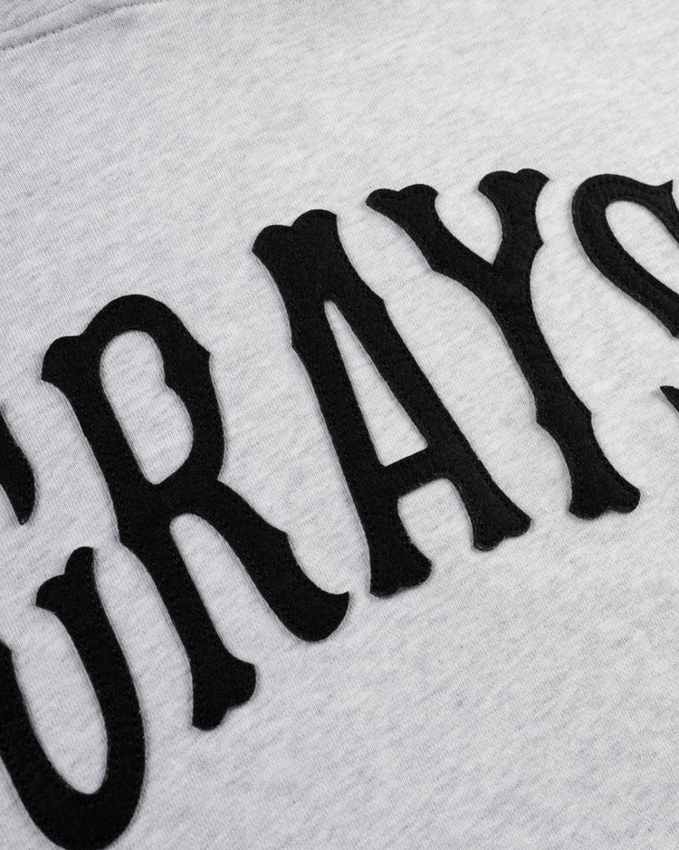 Close-up of black, raised letters spelling GRAYS on light gray fabric, part of the Homestead Grays Heavyweight Cotton Terry Pullover Hoodie by Ebbets Field Flannels, inspired by the Negro Leagues Baseball Museum.