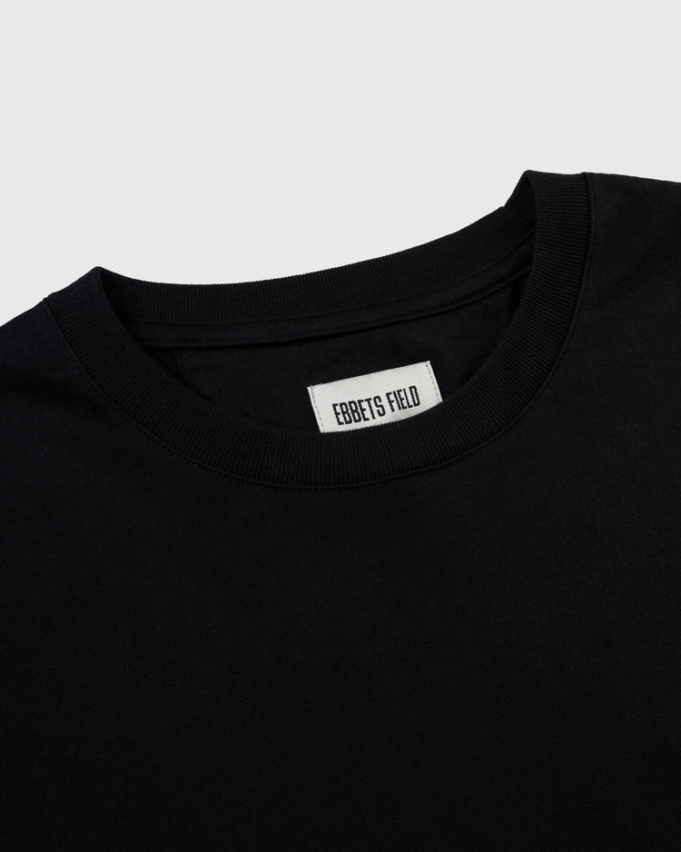 Close-up of the Homestead Grays Embroidered G Short Sleeve Tee by Ebbets Field Flannels, a plain black crew-neck with a visible white EBBETS FIELD label inside the collar, shown on a light gray background.