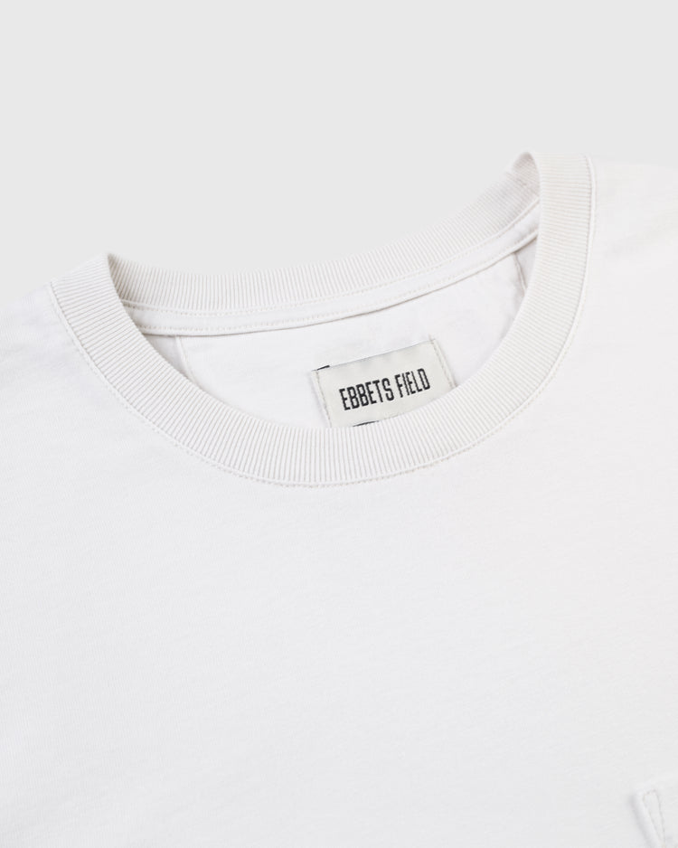 A close-up of the collar and neck label of the Ebbets Field Flannels Homestead Grays Embroidered G Long Sleeve Pocket Tee, with a visible tag. The light gray background highlights this tribute to the legendary team.