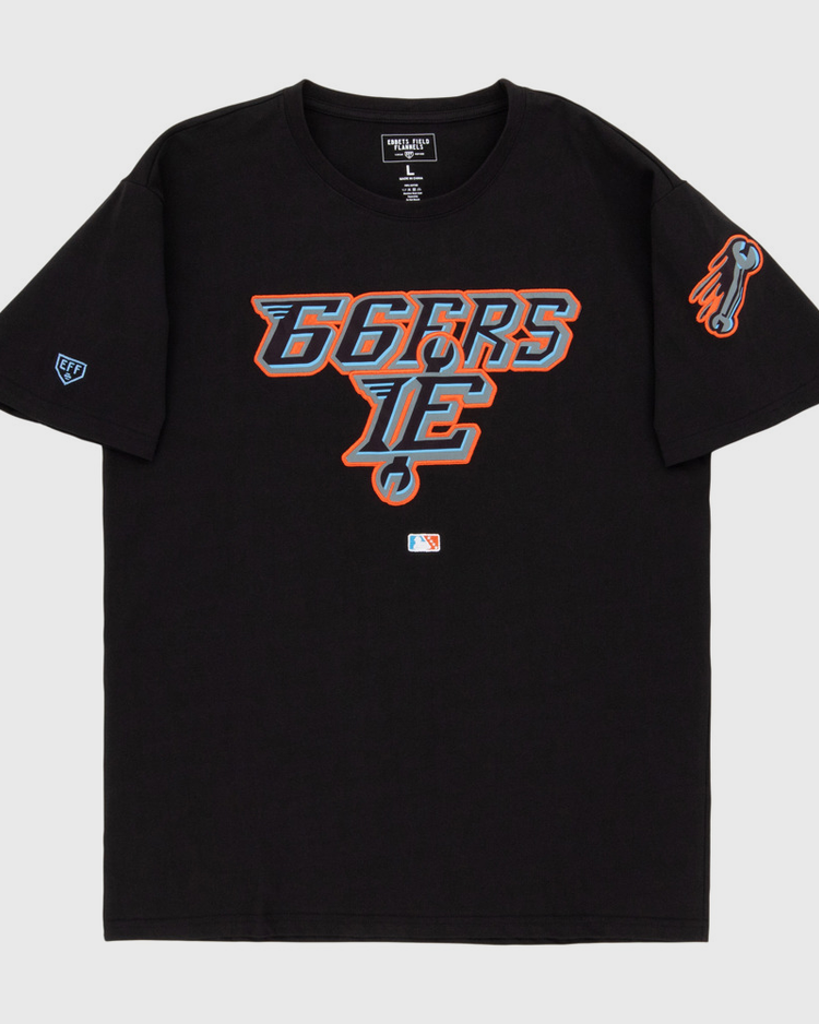 The Ebbets Field Inland Empire 66Ers MiLB Fashion Cotton Short Sleeve Tee features a black design with a blue, orange, and white stylized 66ERS IE logo on the chest, a flaming baseball graphic on the sleeve, and an official MLB logo near the hem.