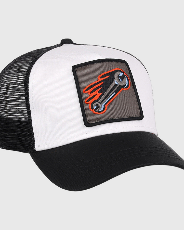 The Inland Empire 66Ers MiLB Trucker Ballcap by Ebbets Field is a black and white hat with a mesh back and a front patch showing a flaming wrench on a gray background.