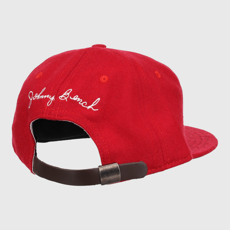 The Ebbets Field Flannels Johnny Bench Signature Series Ballcap is a red vintage wool cap with white embroidered cursive, inspired by Johnny Bench, and has an adjustable brown strap with a metal buckle at the back.