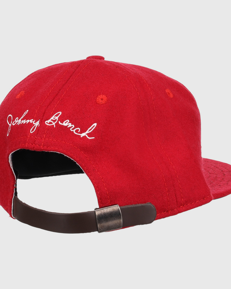 The Ebbets Field Flannels Johnny Bench Signature Series Ballcap is a red vintage wool cap with white embroidered cursive, inspired by Johnny Bench, and has an adjustable brown strap with a metal buckle at the back.