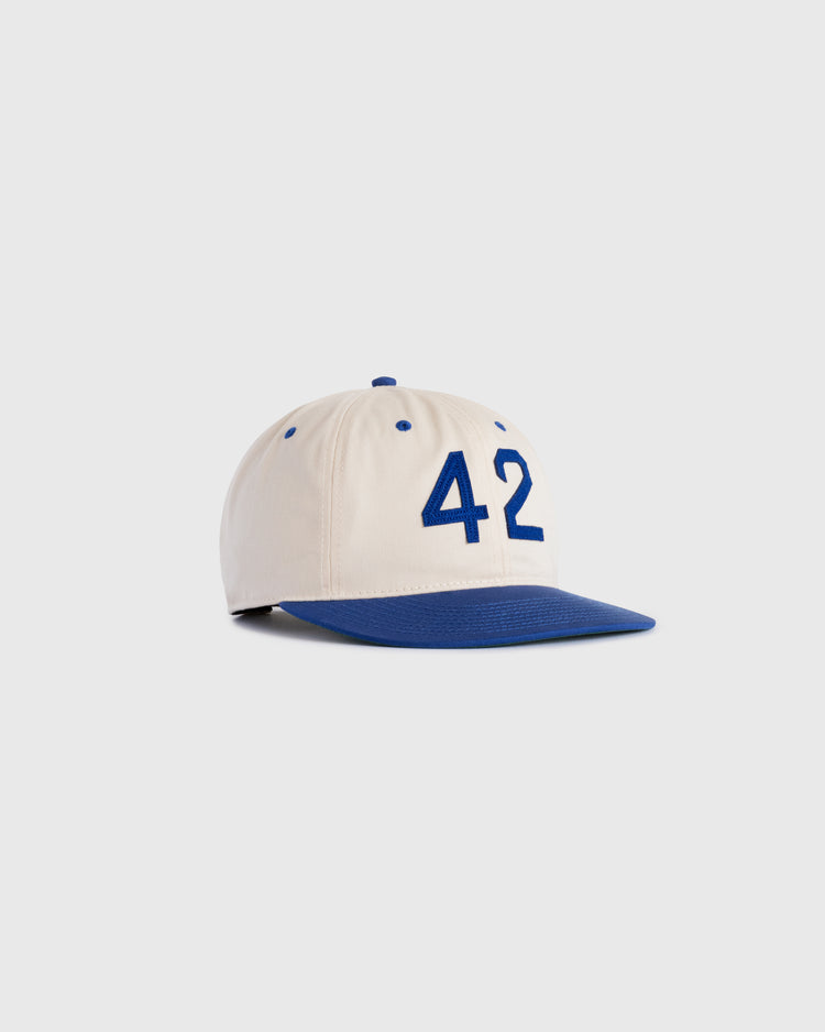 The Ebbets Field Jackie Robinson Day ‘42’ Cotton Twill Ballcap features a cream color, blue brim, and bold blue 42 on the front, honoring baseball legacy, showcased on a plain light background.