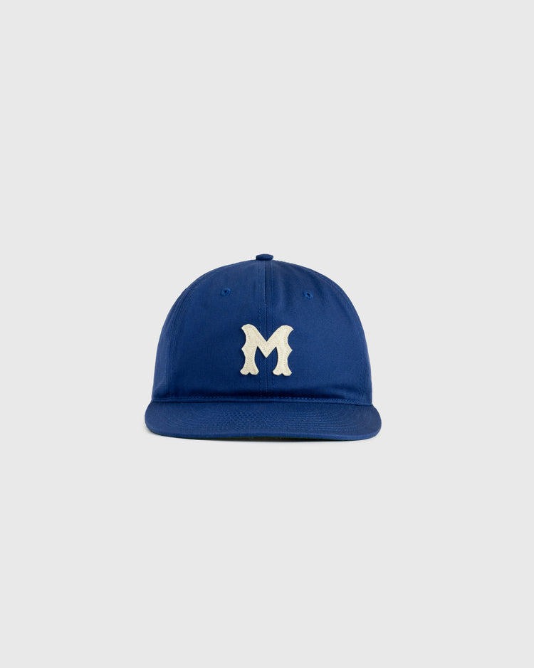 The Jackie Robinson Day Montreal Royals ‘M’ Cotton Twill Ballcap by Ebbets Field features a blue cap with a white stylized M on the front, shown against a plain light gray background.