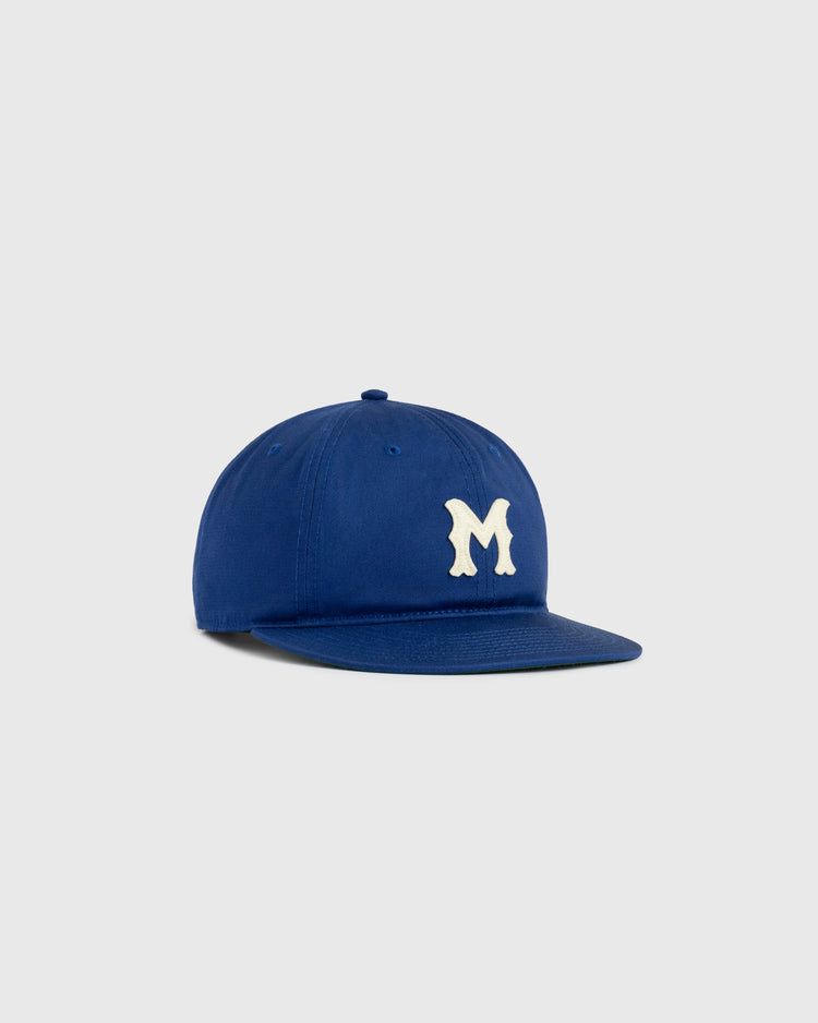 The Ebbets Field Jackie Robinson Day Montreal Royals ‘M’ Cotton Twill Ballcap in royal blue features a crisp white letter M on the front and is displayed against a plain light gray background.