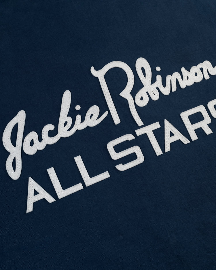 Close-up of the Jackie Robinson Cotton Grounds Crew Jacket by Ebbets Field, a navy blue baseball jacket featuring white “Jackie Robinson ALL STARS” script and block lettering.