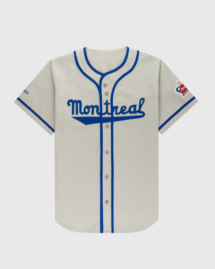 The Ebbets Field Montreal Royals Cotton Twill Baseball Jersey features gray fabric, blue trim and buttons, Montreal in blue script on the chest, and a left-sleeve patch with red and gold accents inspired by Jackie Robinson.