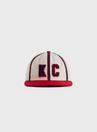 The EFF Kansas City Monarchs 1942 Authentic Wool Ballcap is a white cap with red trim and brim, featuring large blue-outlined red KC letters, inspired by the original Negro Leagues Baseball Museum design.