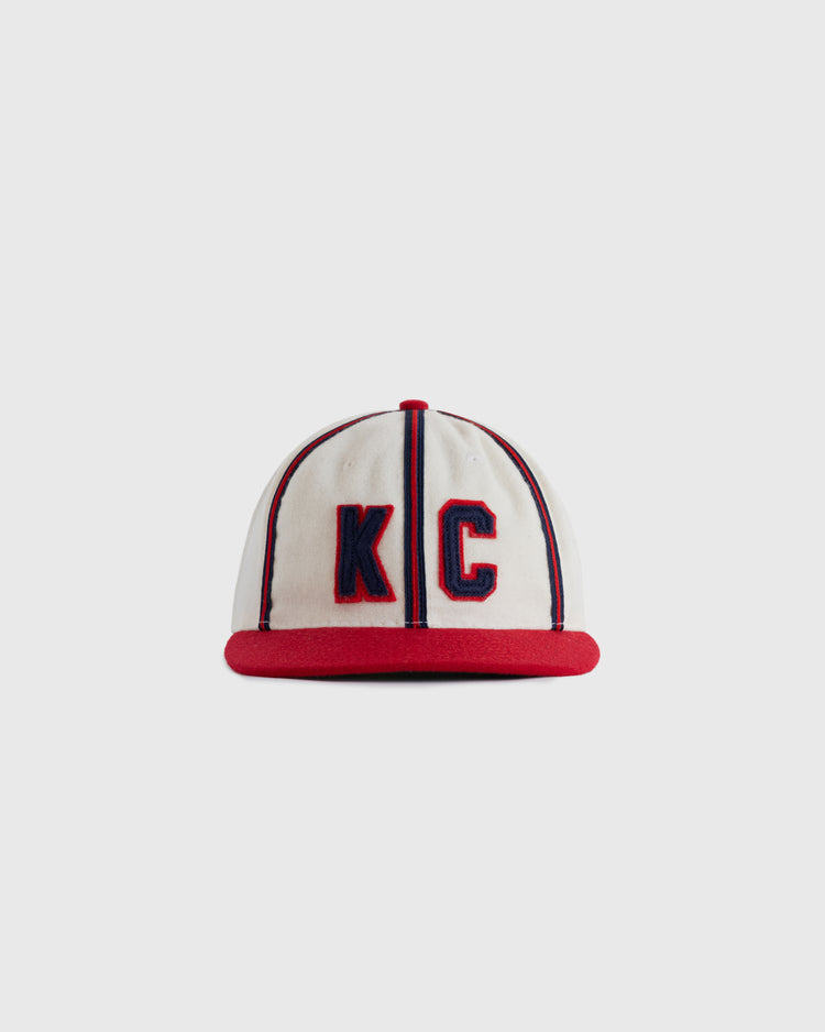 The EFF Kansas City Monarchs 1942 Authentic Wool Ballcap is a white cap with red trim and brim, featuring large blue-outlined red KC letters, inspired by the original Negro Leagues Baseball Museum design.