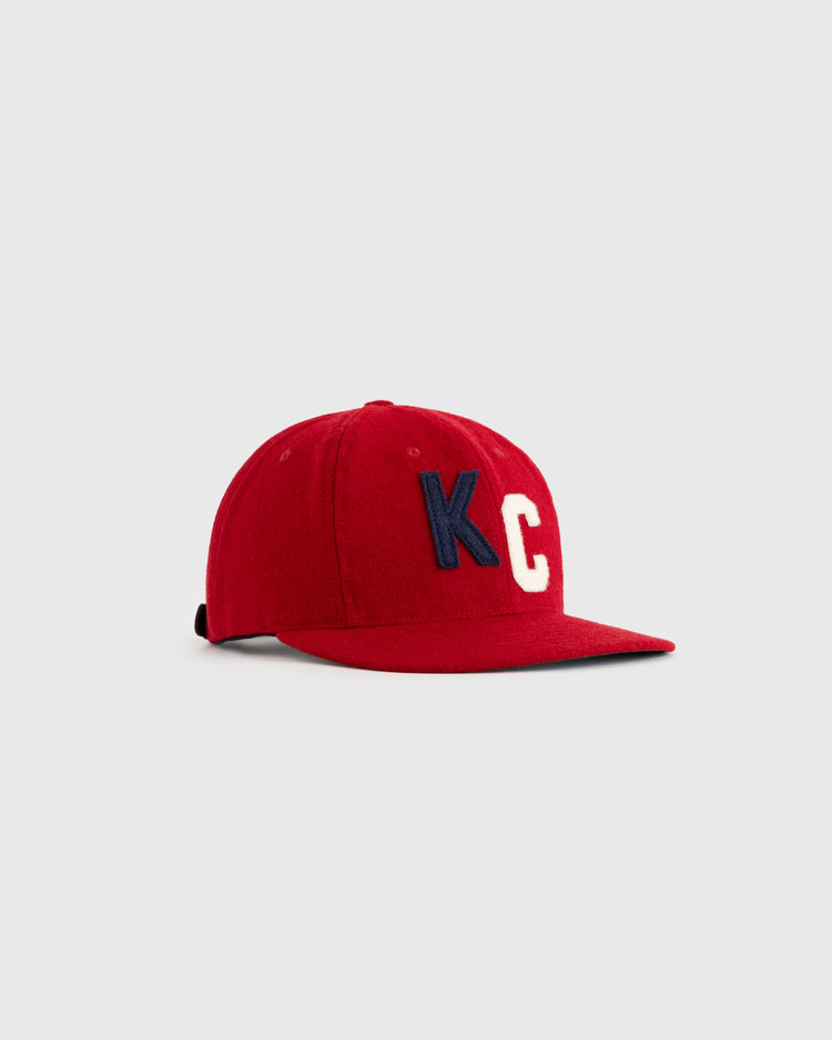 The EFF Kansas City Monarchs 1936 Authentic Wool Ballcap is a red, flat-brim cap featuring large blue and white KC embroidery on the front, inspired by the original 1936 design, shown against a plain light gray background.