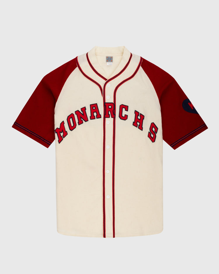 The Ebbets Field Kansas City Monarchs 1942 Authentic Wool Home Baseball Jersey features a cream body with red sleeves and piping, MONARCHS across the chest, and a left sleeve patch honoring Negro Leagues Baseball heritage.