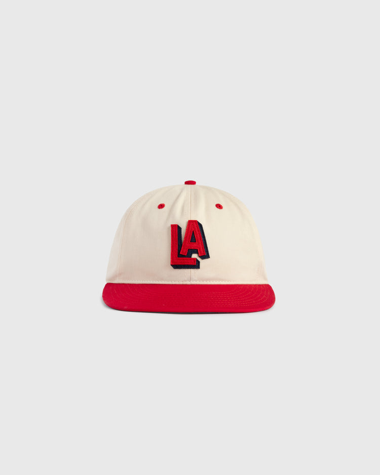 The Ebbets Field Los Angeles Angels (PCL) 1942 Logo Cotton Twill Ballcap features a cream cotton twill body, red brim and button, and bold red-and-black embroidered LA letters. Inspired by the 1942 team cap. Set on a light gray background.