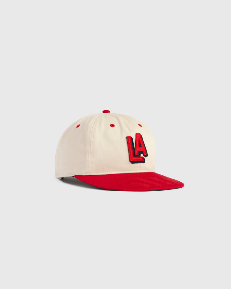 The Ebbets Field Los Angeles Angels (PCL) 1942 Logo Cotton Twill Ballcap features a beige crown, red brim, button, and eyelets, with bold raised red and black LA letters on the front. Displayed on a plain light gray background.