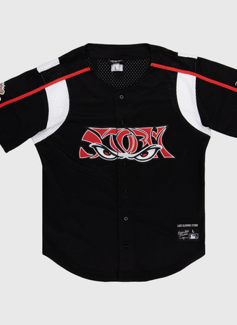 The Ebbets Field Lake Elsinore Storm MiLB Button Down Jersey is a black short-sleeve baseball jersey with white and red accents, mesh panels, a stylized eyes logo on the chest, and patches on the left sleeve and lower right front.