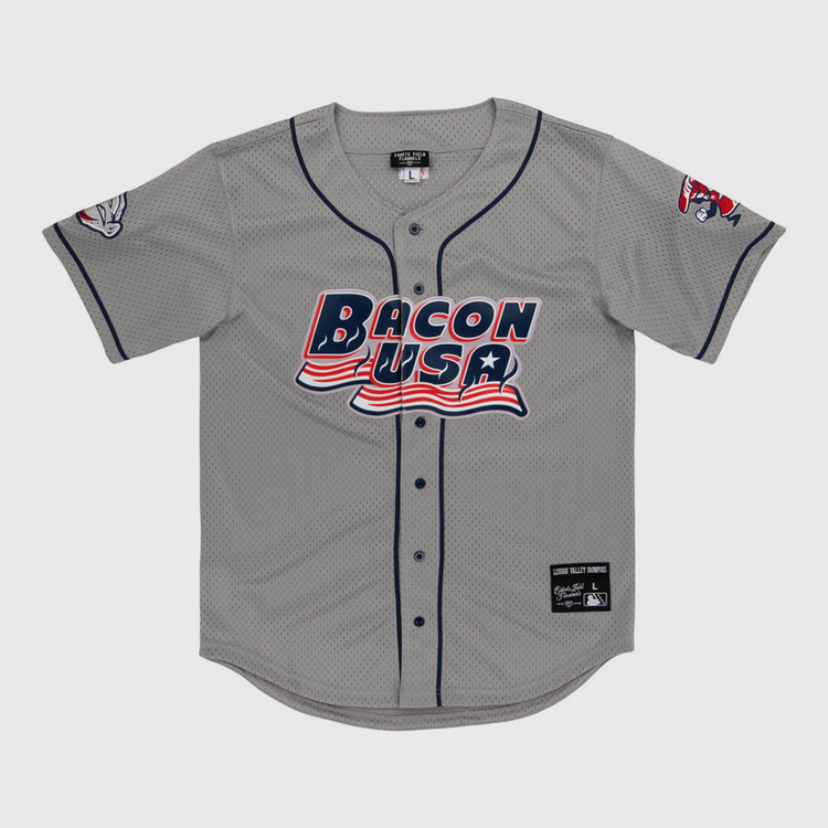 The Lehigh Valley Ironpigs MiLB Button Down Jersey by Ebbets Field is a gray baseball jersey with navy trim, “Bacon USA” in red, white, and blue on the front, plus cartoon bacon designs on the left sleeve and right shoulder.
