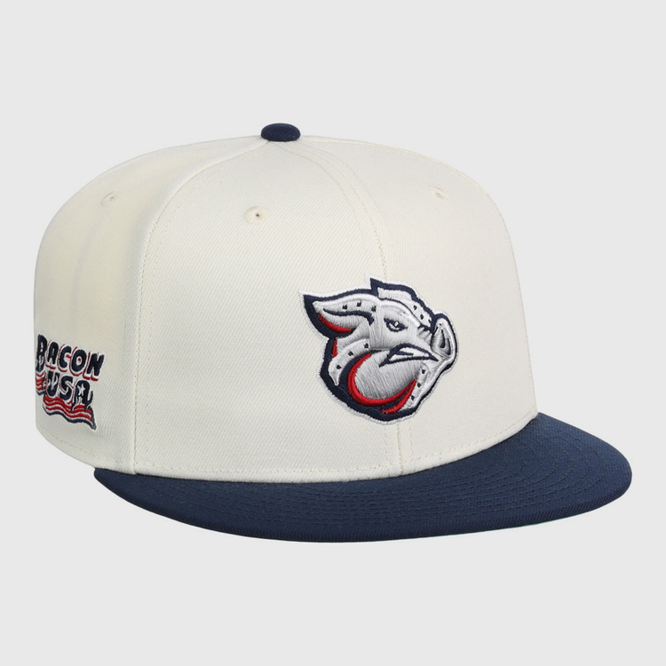 The Lehigh Valley Ironpigs MiLB Snapback Ballcap by Ebbets Field features a cream crown, navy brim, stylized pig logo on the front, and Bacon USA text with an American flag graphic on the side.