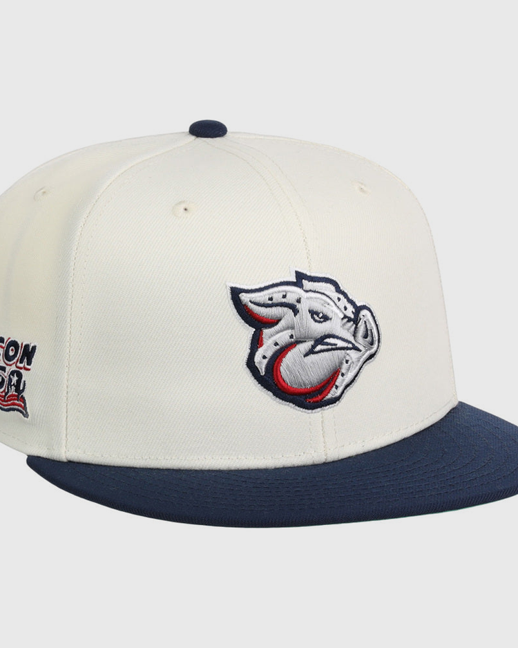 The Lehigh Valley Ironpigs MiLB Snapback Ballcap by Ebbets Field features a cream crown, navy brim, stylized pig logo on the front, and Bacon USA text with an American flag graphic on the side.