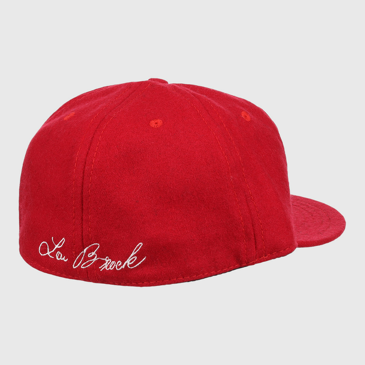 The Ebbets Field Flannels Lou Brock Signature Series Ballcap is a vintage red wool cap, shown from the back left, with Lou Brock’s signature in white cursive embroidered above the band.