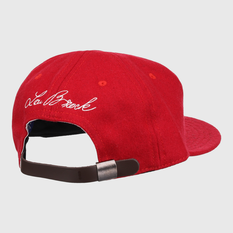The Ebbets Field Flannels Lou Brock Signature Series Ballcap is a red vintage wool cap with a brown adjustable strap and metal clasp. White cursive embroidery of the Lou Brock signature appears on the left side.
