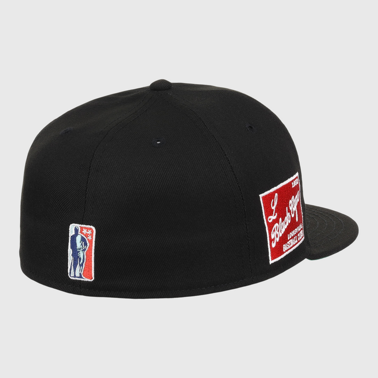 The EFF Louisville Black Caps NLB Team Color Fitted Ballcap is a black vintage cap with an embroidered blue and white silhouette patch on the left and a red and white patch on the back, celebrating the Negro National League legacy.