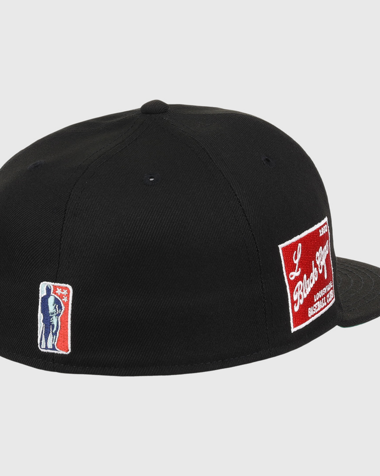 The EFF Louisville Black Caps NLB Team Color Fitted Ballcap is a black vintage cap with an embroidered blue and white silhouette patch on the left and a red and white patch on the back, celebrating the Negro National League legacy.