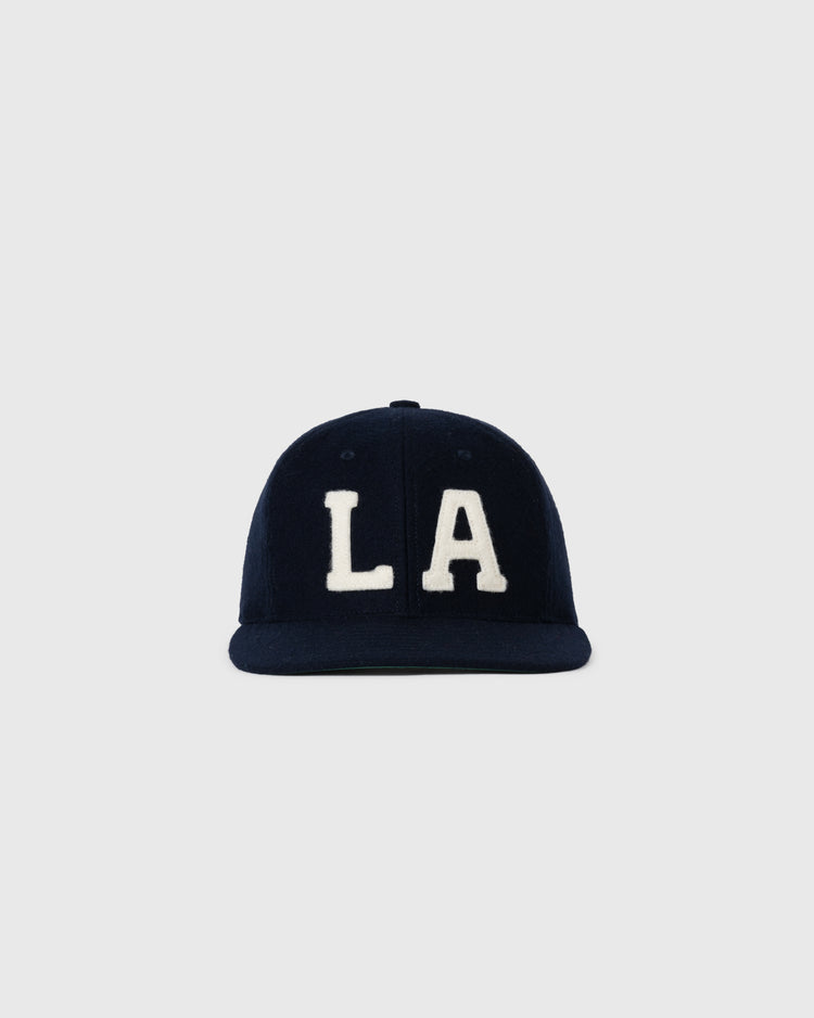 The EFF Los Angeles (PCL) 1949 Authentic Wool Ballcap is a navy blue cap featuring bold white “LA” letters, inspired by the Pacific Coast League Angels, shown against a plain light gray background.