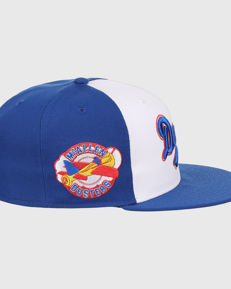 The EFF McAllen Dusters Lone Star Fitted Ballcap features blue and white panels, a flat blue brim, and a colorful yellow airplane patch with HEALEN DUSTERS embroidered, inspired by the classic Lone Star League team.