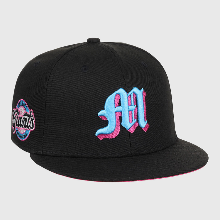 The EFF Miami Giants NLB Team Color Fitted Ballcap is a vintage-inspired black cap with a bold blue and pink M on the front and a matching embroidered San Francisco Giants team logo patch on the side.