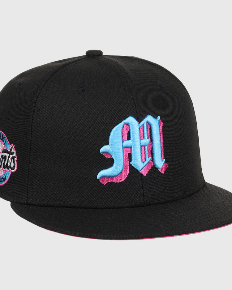 The EFF Miami Giants NLB Team Color Fitted Ballcap is a vintage-inspired black cap with a bold blue and pink M on the front and a matching embroidered San Francisco Giants team logo patch on the side.