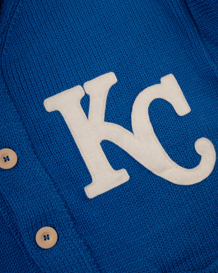 Close-up of the Kansas City Royals 1969 Wool Shawl Collar Sweater by Ebbets Field Flannels, a blue knit MLB sweater with beige buttons and bold white KC letters, inspired by vintage on-field designs.