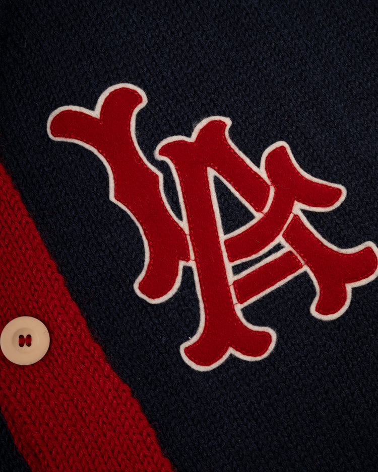 Close-up of a navy blue wool LA Angels 1961-65 Shawl Collar Sweater by Ebbets Field Flannels, featuring interlocking red and white LA letters, a red stripe, and a beige button on the left side.