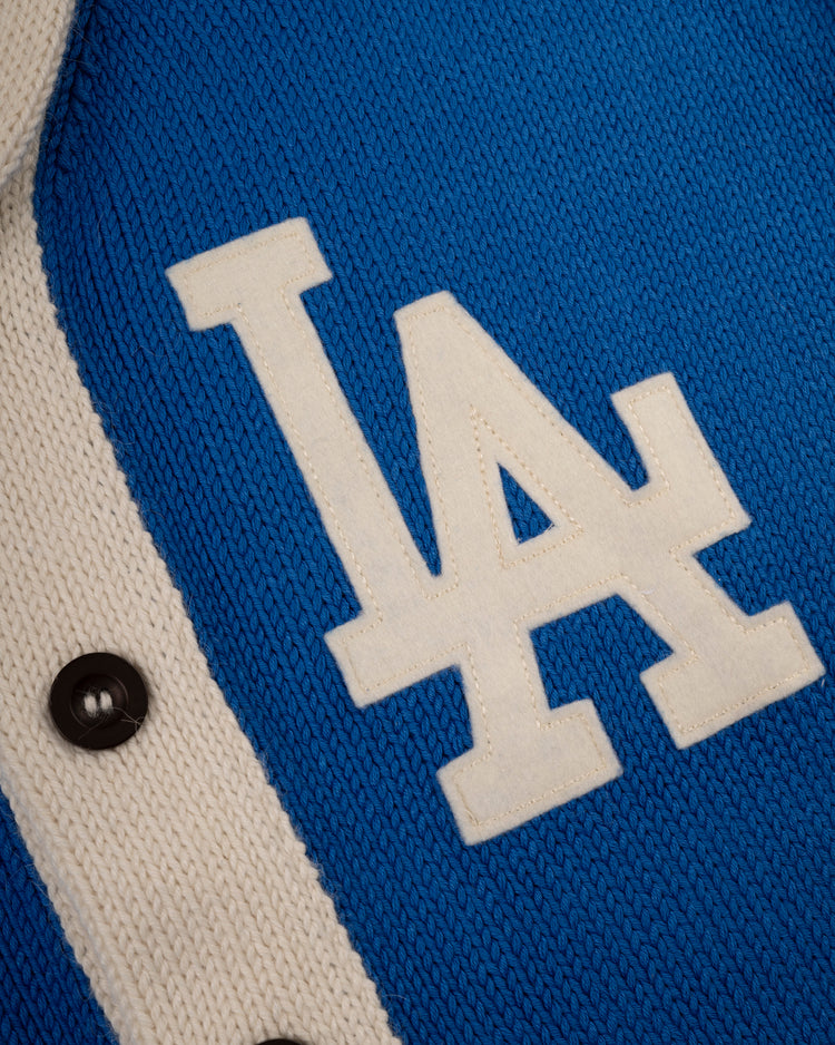 Close-up of the blue and white LA Dodgers 1958 Wool Shawl Collar Sweater by Ebbets Field Flannels, featuring a white LA logo and black buttons on the left side—a classic MLB sweater style.