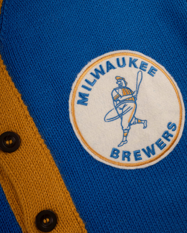 Close-up of the Milwaukee Brewers 1970-1977 Wool Shawl Collar Sweater by Ebbets Field Flannels, featuring blue and yellow knit, black buttons, and a round patch with a swinging baseball player—ideal for fans seeking classic replica styles.