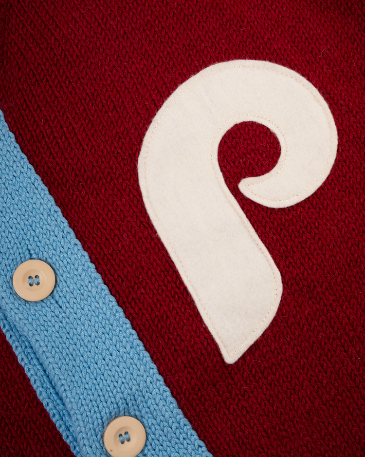 Close-up of the Philadelphia Phillies 1979 Wool Shawl Collar Sweater by Ebbets Field Flannels, featuring red knit, a large white P patch, light blue trim, and beige buttons reminiscent of classic on-field Phillies style.