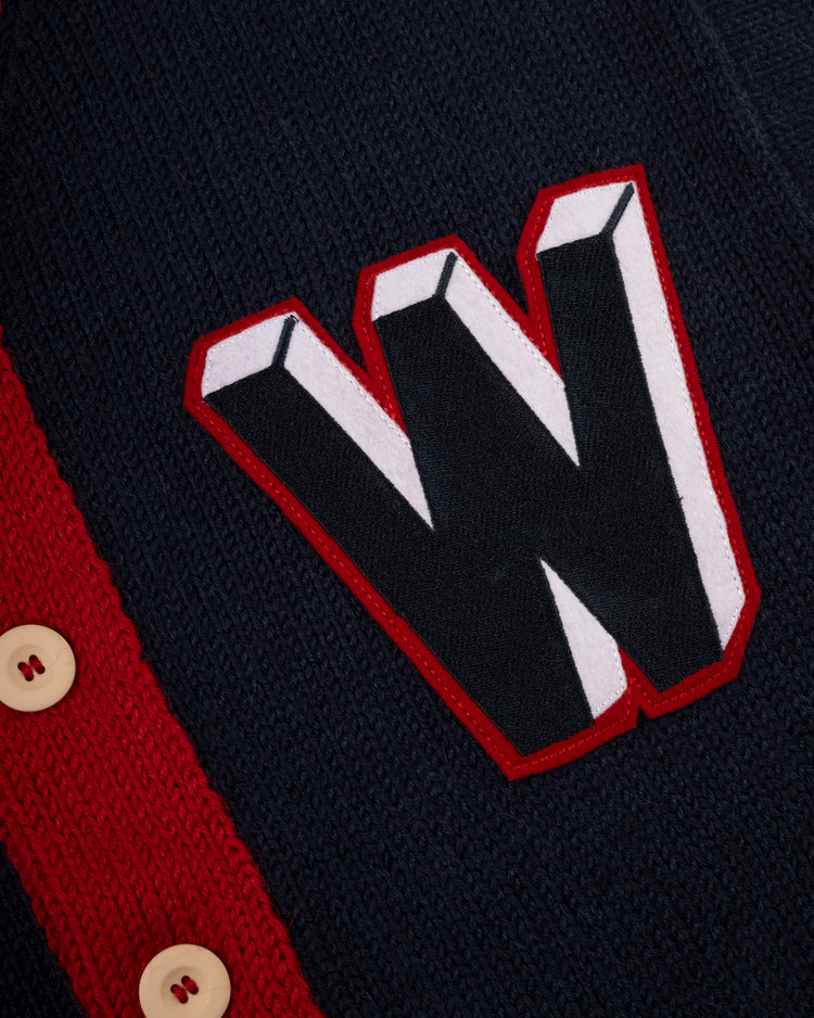 A close-up of the Ebbets Field Flannels Washington Senators 1963-67 Wool Shawl Collar Sweater, featuring navy knit fabric, cream buttons, and a bold W patch outlined in red and white, inspired by classic team baseball sweaters.