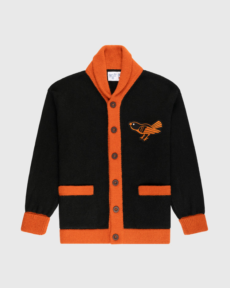 The Ebbets Field Flannels Baltimore Orioles 1964-65 Wool Shawl Collar Sweater is black with orange trim, cuffs, and pockets. It features an orange bird on the left chest, brown buttons, and a vintage-inspired shawl-collar design.