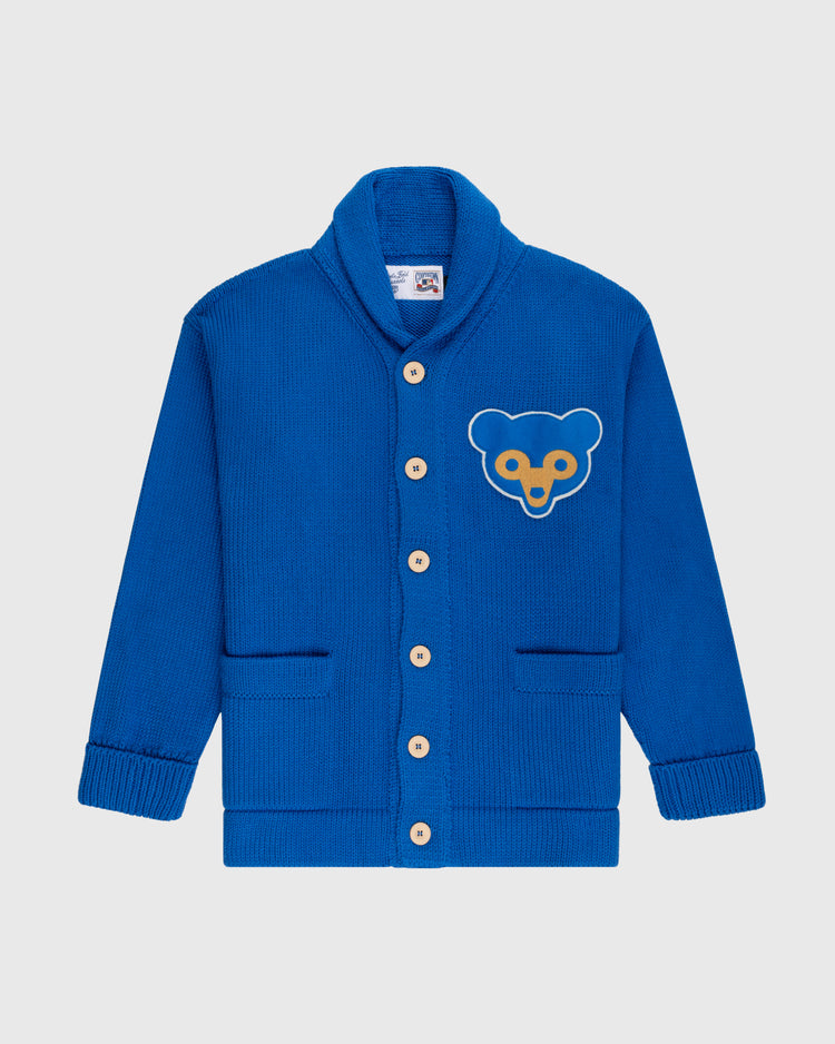 The Ebbets Field Flannels Chicago Cubs 1962 Wool Shawl Collar Sweater features wooden buttons, two front pockets, and a yellow and blue bear face patch on the left chest, inspired by a classic Cubs replica baseball sweater. Shown on a white background.