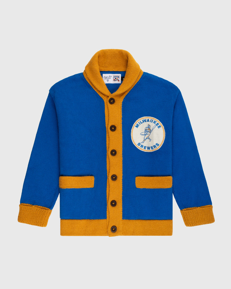 The Ebbets Field Flannels Milwaukee Brewers 1970-1977 Wool Shawl Collar Sweater features blue and gold colors, brown buttons, gold trim, and a chest patch reading MILWAUKEE BREWERS with a baseball player graphic.