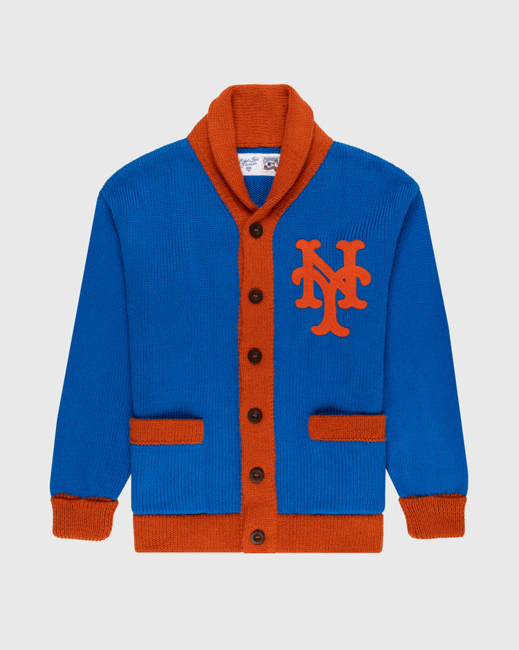 The Ebbets Field Flannels New York Mets 1962 Wool Shawl Collar Sweater features blue wool with orange trim, buttons, pockets, and a bold NY chest logo. This replica baseball sweater is displayed on a plain light background.