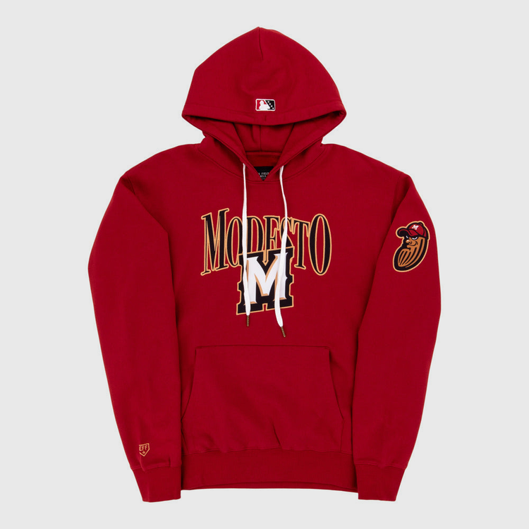 The Ebbets Field Modesto Nuts MiLB Cotton Hooded Sweatshirt is a red hoodie with MODESTO and a large gold and white M on the front, a red bird head patch on the left sleeve, and an MLB logo on the hood.