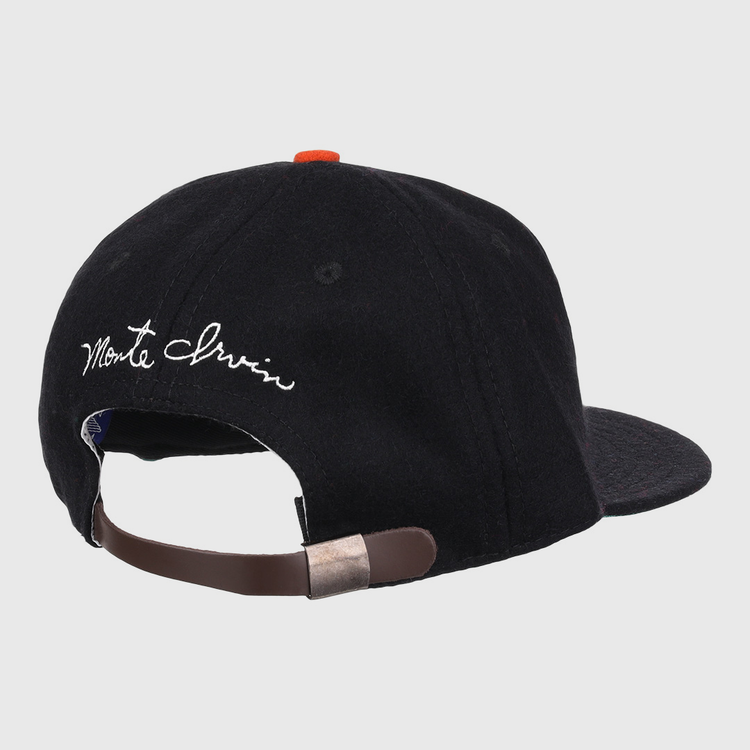 A black wool ballcap by Ebbets Field Flannels, the Monte Irvin Signature Series, shown from the back with an adjustable brown strap, metal clasp, and white cursive Monte Irvin above the opening—evoking classic Negro National League styles.