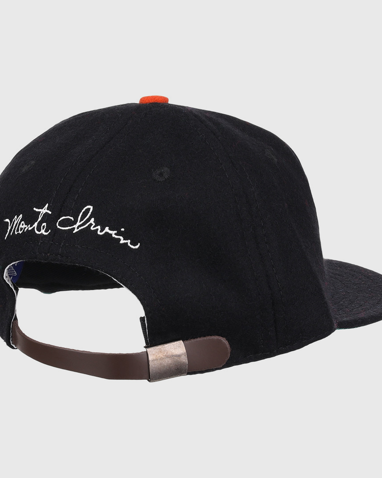A black wool ballcap by Ebbets Field Flannels, the Monte Irvin Signature Series, shown from the back with an adjustable brown strap, metal clasp, and white cursive Monte Irvin above the opening—evoking classic Negro National League styles.