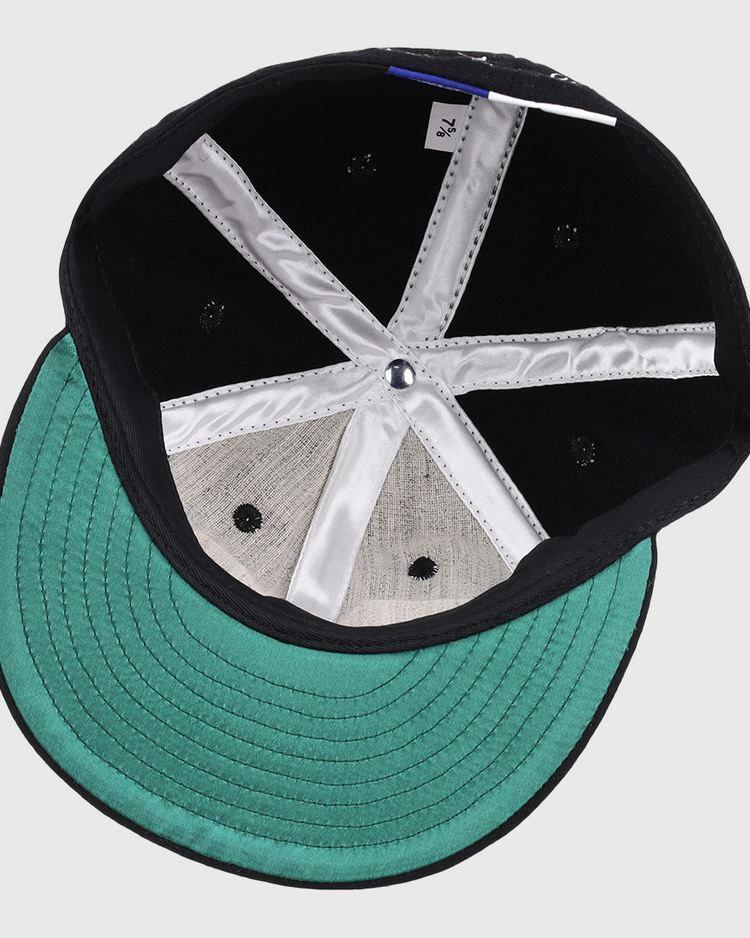 The image displays the inside of an Ebbets Field Flannels Monte Irvin Signature Series Ballcap, featuring a green underbrim, silver fabric lining, black rivets in the crown, and a white size tag—evoking early Negro National League styles.