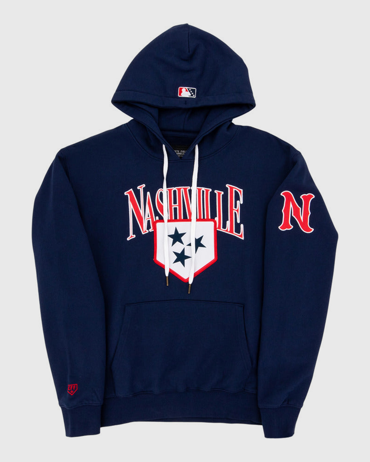 The Ebbets Field Nashville Sounds MiLB Cotton Hooded Sweatshirt is a navy blue hoodie with white drawstrings, Nashville in bold white and red letters, a three-star shield on the chest, red N on the sleeve, and an MLB logo on the hood.