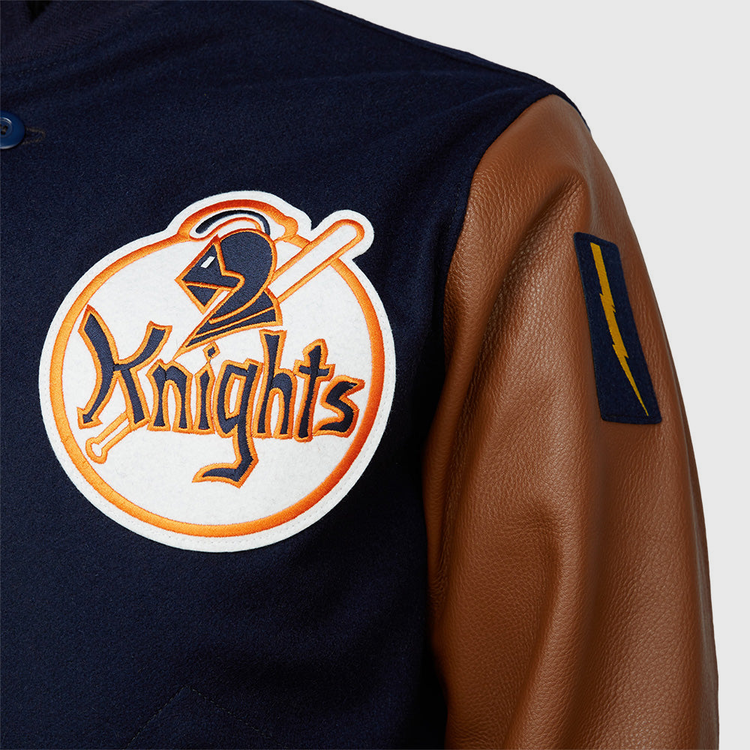 A close-up of the EFF New York Knights 1939 Authentic Jacket, crafted from melton wool with brown leather sleeves, featuring a large chest patch of a knight’s helmet and bat, plus a blue patch with a yellow lightning bolt on the sleeve.