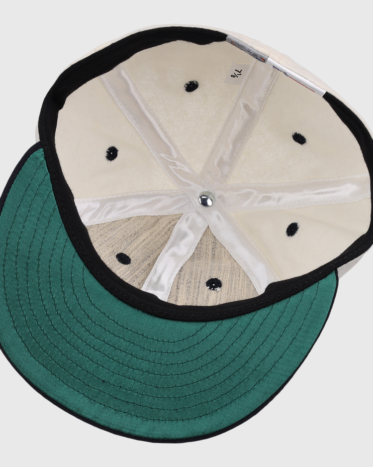 A look inside the Ebbets Field Flannels New York Rens Wool Ballcap, featuring a green underbill, black trim, visible stitching, and metal top button. The size label reads 7 1/2—classic vintage style.