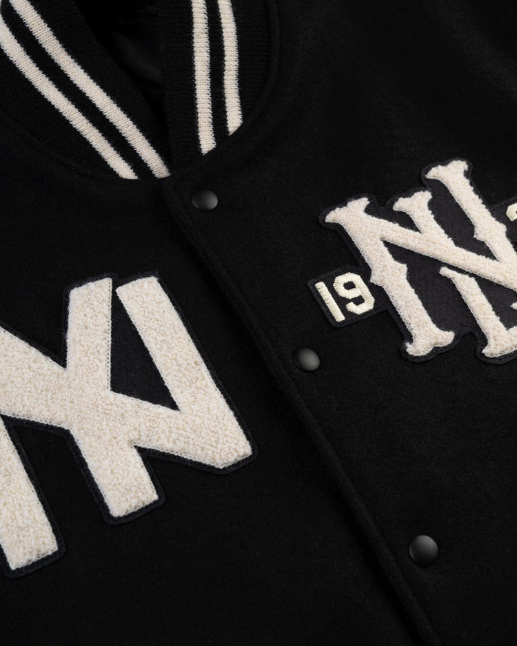 Close-up of the Ebbets Field Negro League Wool & Leather Varsity Jacket, featuring white snap buttons, textured white NY and 19 patches, and a black-and-white striped ribbed collar.
