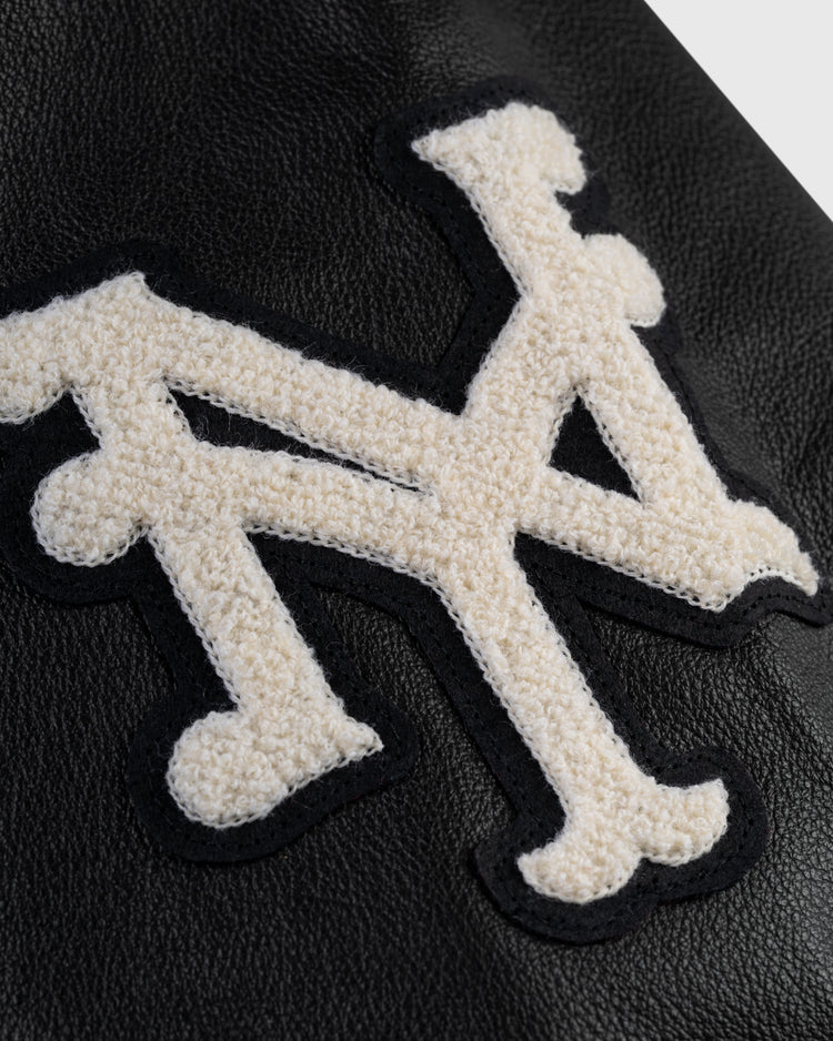 A cream NY patch in vintage font is stitched onto black leather on the Ebbets Field Negro League Wool & Leather Varsity Jacket, inspired by classic Negro Leagues varsity styles.